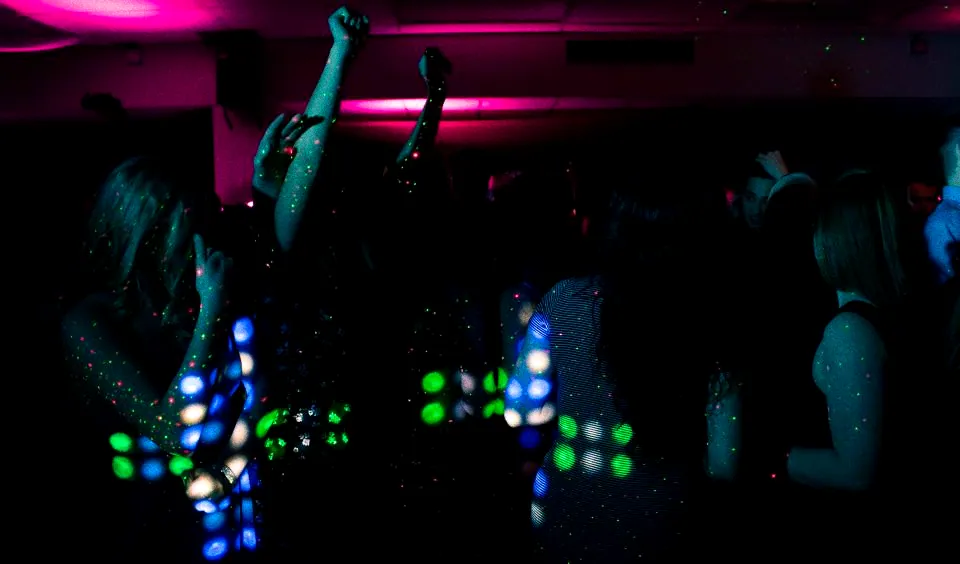 A dark room full of people dancing under green and pink light