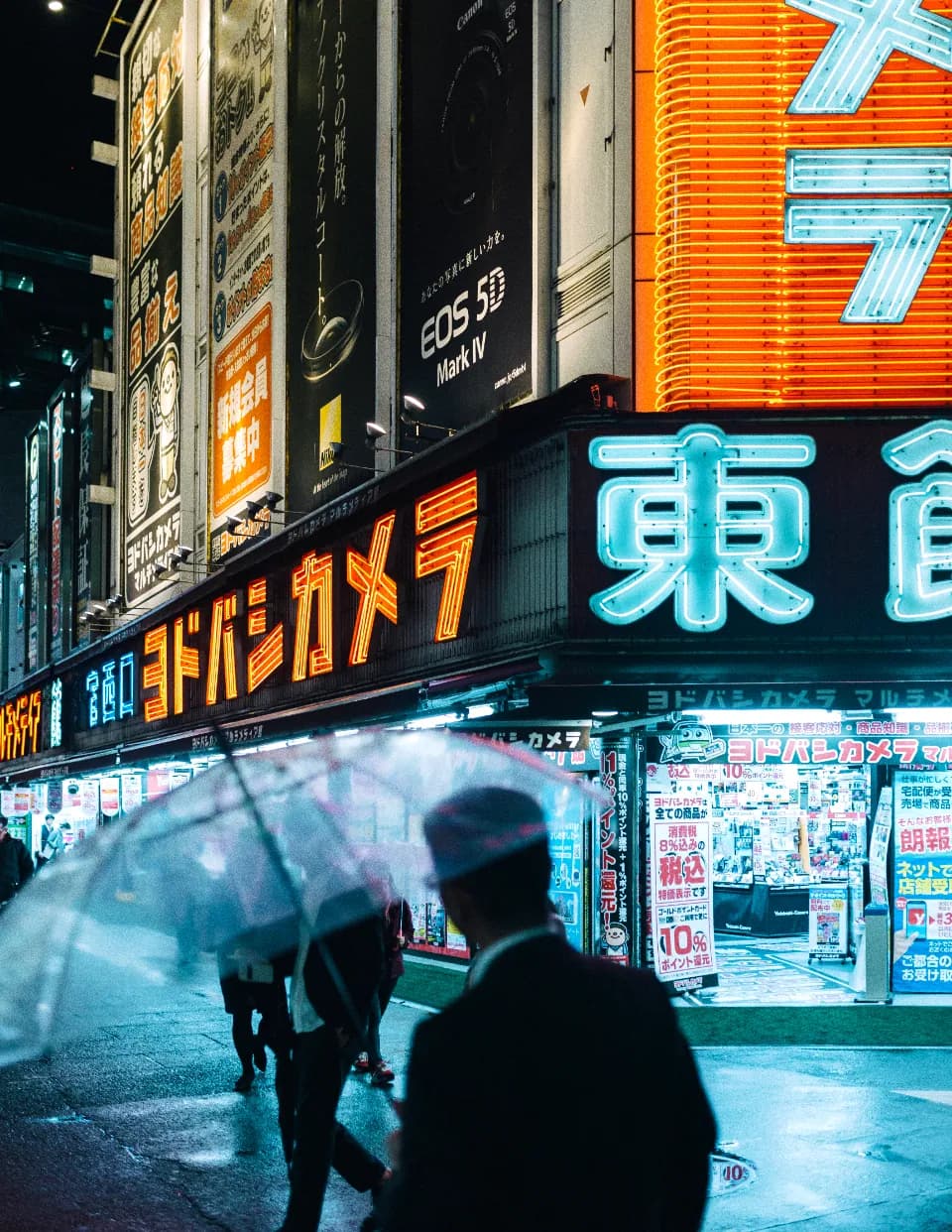 Neon shopfront signs stacked up a building on a rainy night, a clear umbrella in the foreground