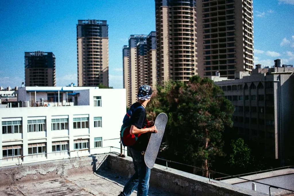 A person holding a skateboard on a rooftop with tower blocks behind