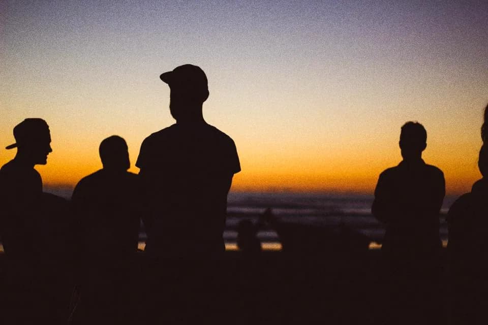 Silhouettes of friends standing together against a fading sky