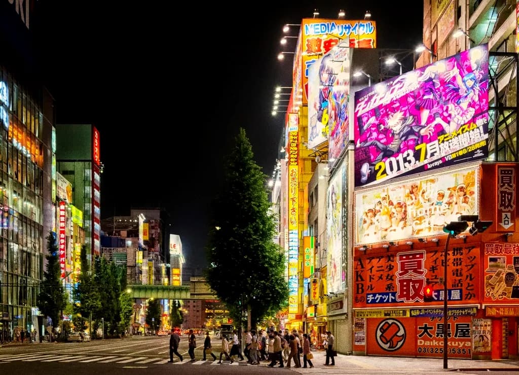 People walking a neon-lit street lined with trees at night