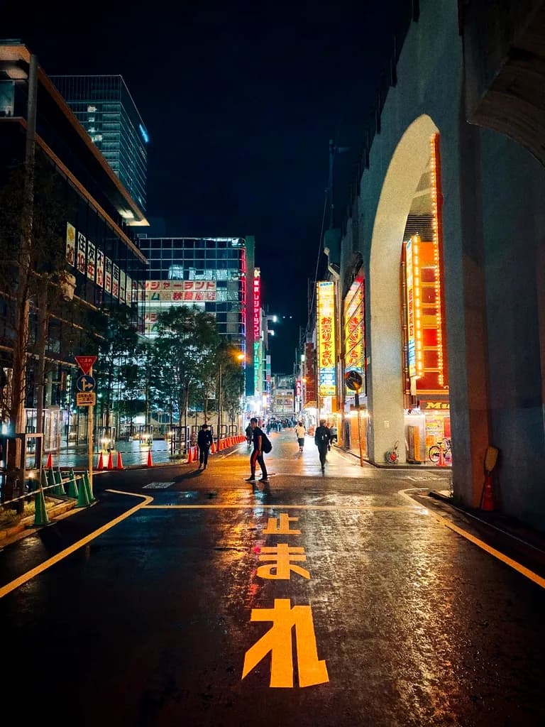 A lone figure crossing a wet street reflecting warm neon light